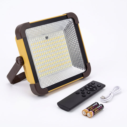 A square LED floodlight with a yellow and dark brown frame, shown with a black remote control, a white USB charging cable, and two batteries on a white background.